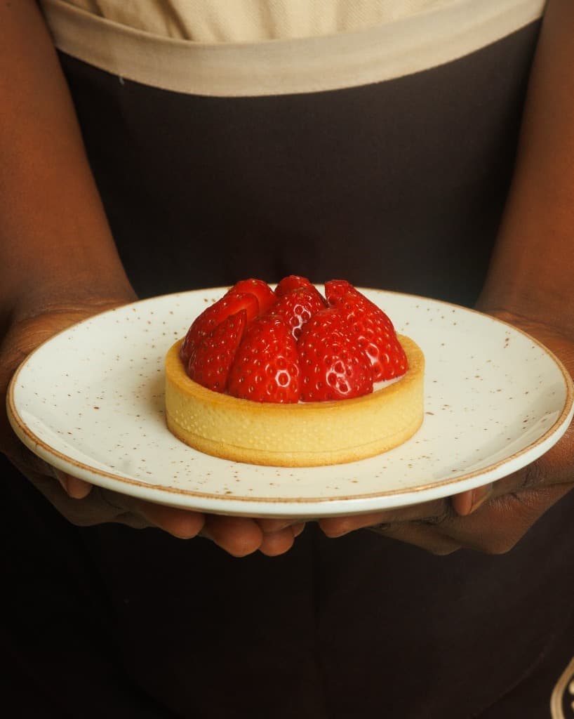 A close-up of a perfectly crafted strawberry tart on a ceramic plate, held in someone's hands.