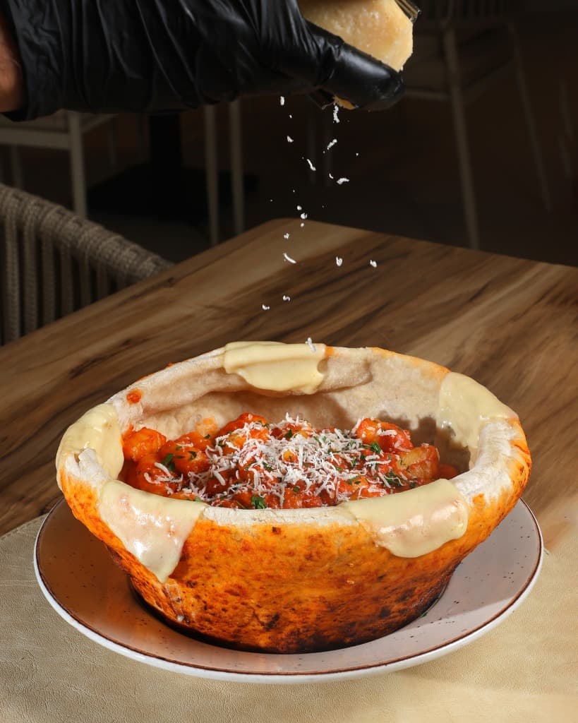 Delicious gnocchi served in a rustic bread bowl with fresh cheese being grated over it.